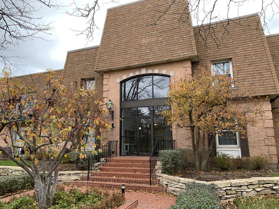 Front view of a large brick building with a prominent entrance and sloped roof.