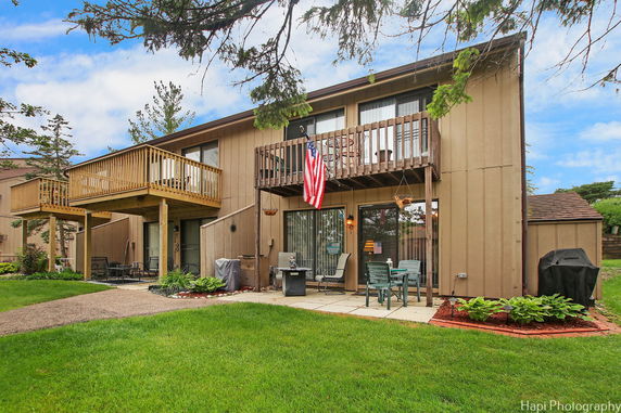 Rear view of a two-story house with wooden balconies and a patio area.