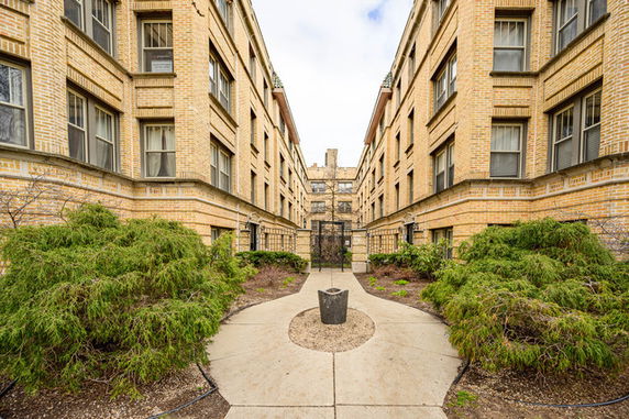 Front view of a multi-story brick apartment building with a walkway and greenery.