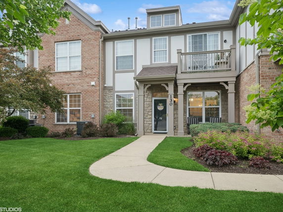 Front view of a two-story brick and stone house with a small porch and balcony.