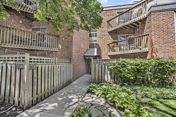 Front view of a brick apartment building with balconies and a wooden fence.