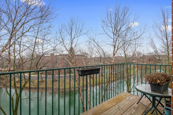 View from a balcony overlooking a river and trees with distant buildings visible.
