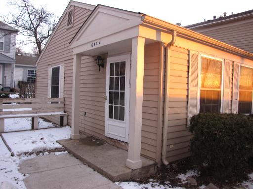 Front view of a small house with a porch entrance in a snowy setting.