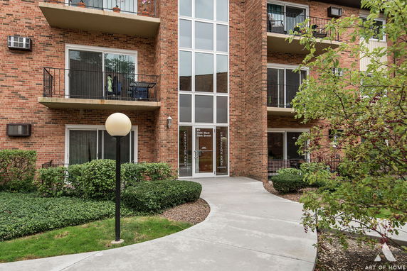 Front view of a brick apartment building with balconies and an entrance with glass doors.