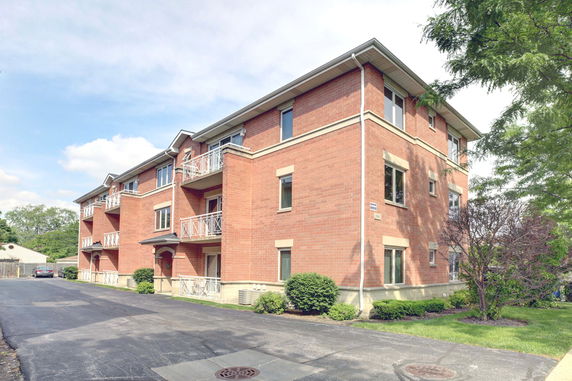 Front view of a three-story brick apartment building with balconies.