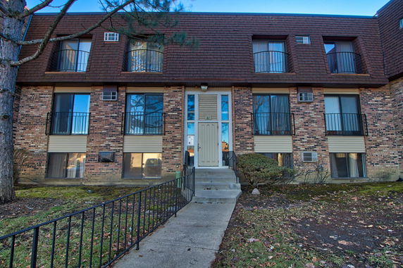 Front view of a multi-story brick apartment building with balconies and a central entrance.