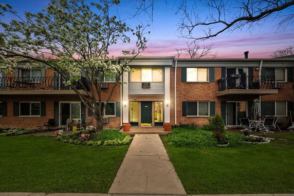 Front view of a two-story brick apartment building with balconies and a landscaped entrance.