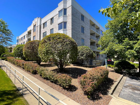 Front view of a multi-story building with balconies and landscaped surroundings.