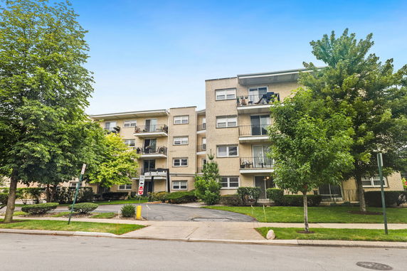 Front view of an apartment building with balconies and surrounded by trees.