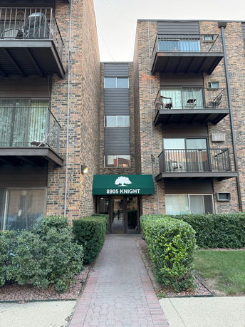 Front view of a brick apartment building with balconies and a green awning over the entrance.
