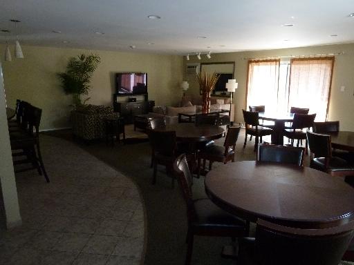 Interior of a clubhouse with multiple round tables and chairs, a TV, and large windows with curtains.