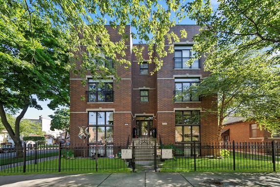 Front view of a multi-story brick building with large windows and a metal fence.
