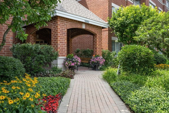 Front view of a brick building entrance with a pathway and surrounding greenery.