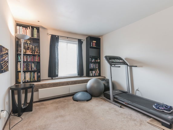 Room with a treadmill, exercise equipment, and bookshelves.