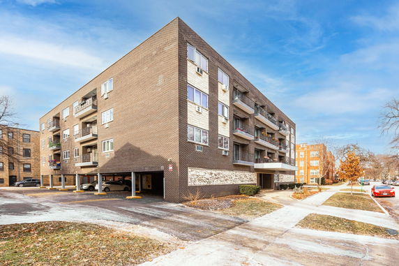 Front view of a multi-story apartment building with balconies and parking area.