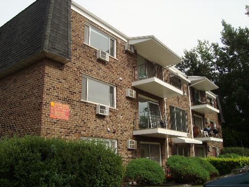Front view of a multi-story brick apartment building with balconies and air conditioning units.