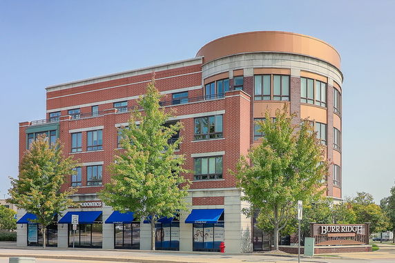 Front view of a multi-story building with a rounded corner section and blue awnings.
