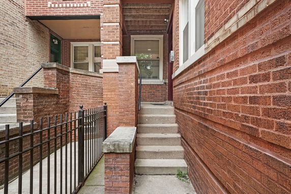 Front view of a brick building entrance with stairs and railing.