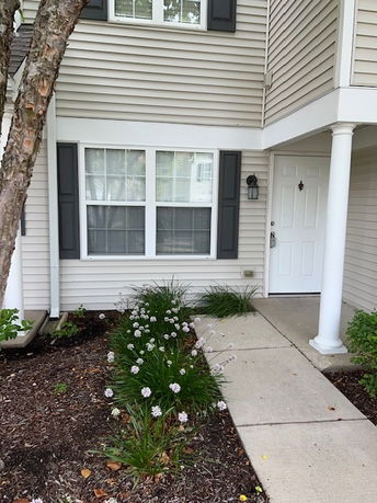 Front view of a house with beige siding and a white door, featuring a small entryway garden.