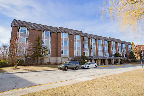 Front view of a multi-story brick building with large windows and a sloped roof.