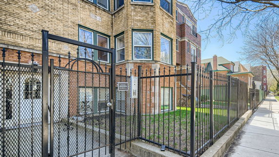 Front view of a multi-story brick building with a black metal fence and entrance gate.