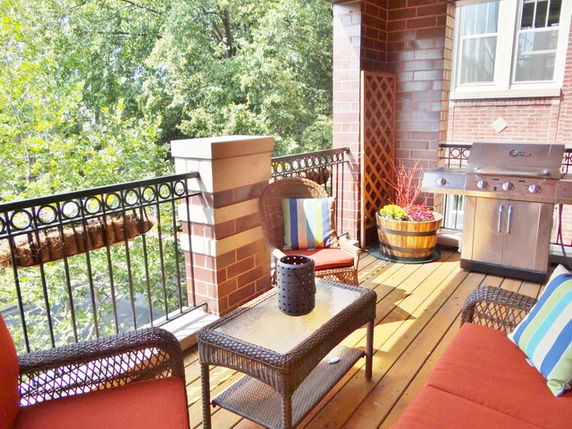 Balcony with outdoor furniture and a grill, overlooking trees.