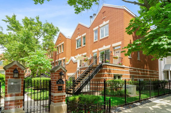 Front view of a multi-story brick townhouse with a gated entrance and stairs leading to the main entrance.