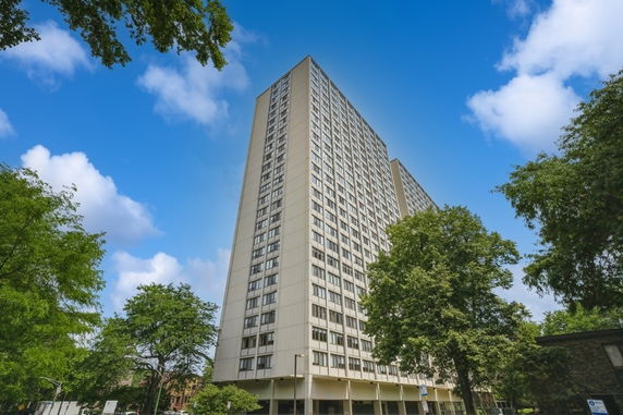 Front view of a tall, multi-story apartment building surrounded by trees.