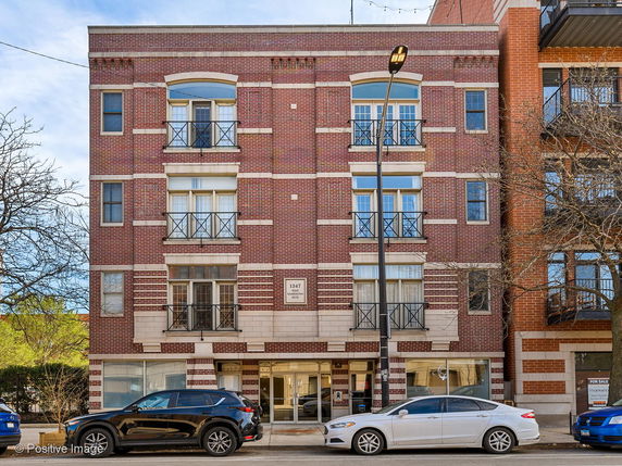 Front view of a multi-story brick building with balconies and large windows.