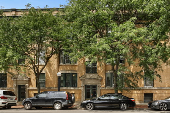 Front view of a multi-story building with trees and parked cars in front.