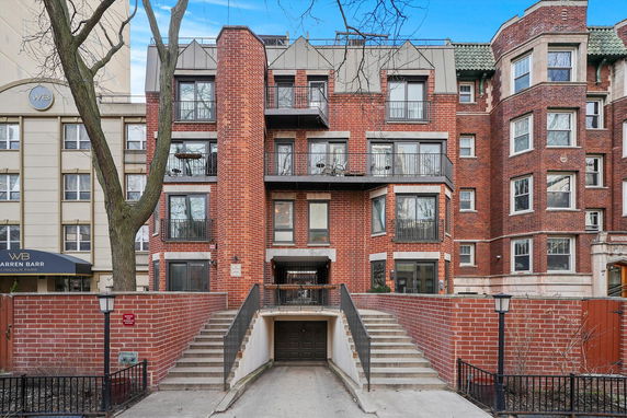 Front view of a multi-story brick apartment building with balconies and a garage entrance.