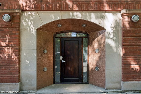 Front view of a building entrance with a wooden door and brick archway.