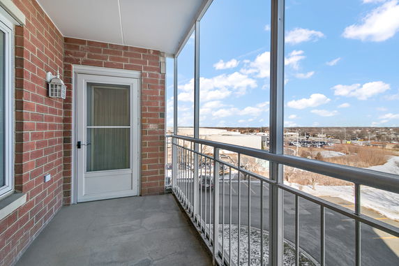 Balcony with brick walls and a white door, offering a view of a parking area and surrounding landscape.
