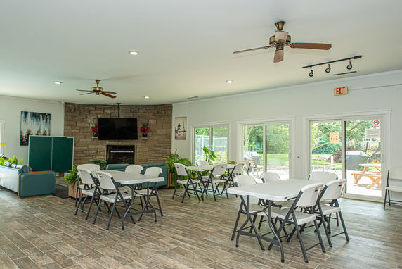 Interior of a clubhouse with tables, chairs, a fireplace, and a TV.