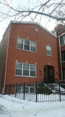 Front view of a brick house with large windows and a fenced yard.