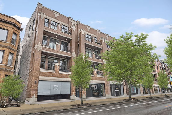 Front view of a multi-story brick building with balconies and retail space on the ground floor.