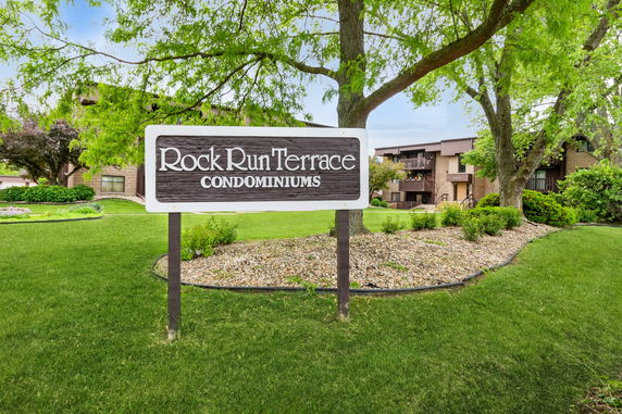 Front view of a condominium complex with a wooden sign reading 'Rock Run Terrace Condominiums'.