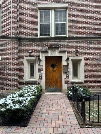 Front view of a brick building entrance with two windows and a wooden door.
