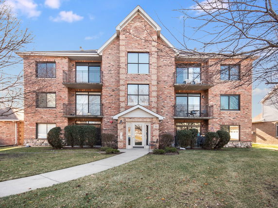 Front view of a three-story brick apartment building with balconies.