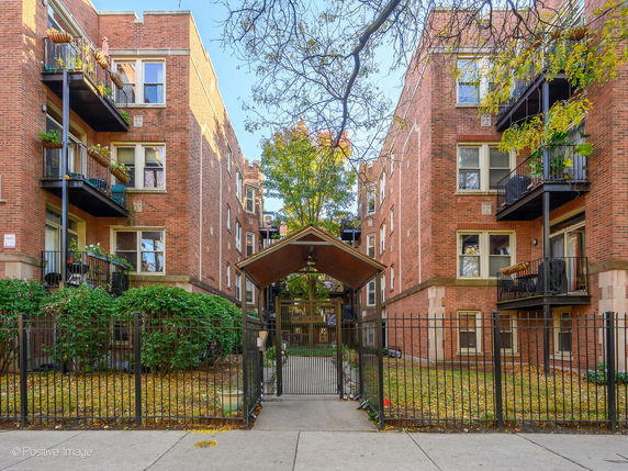 Front view of a multi-story brick apartment building with balconies and a gated entrance.