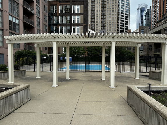 Outdoor swimming pool area surrounded by buildings and a pergola.