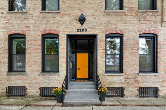 Front view of a brick building with a yellow door and multiple windows.