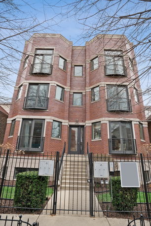Front view of a multi-story brick building with large windows and a gated entrance.