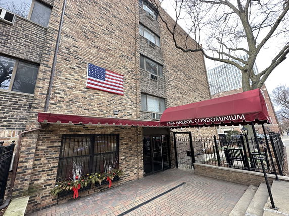 Front view of a multi-story condominium building with a brick exterior and an American flag displayed.