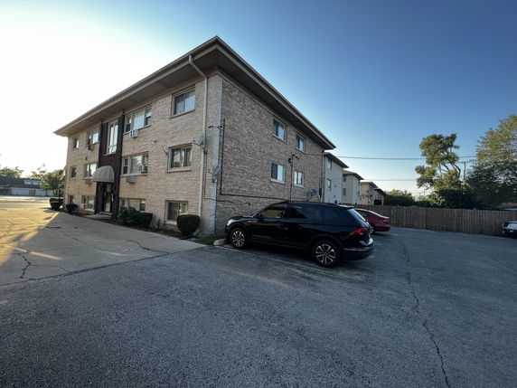 Front view of a three-story brick apartment building with parking area.