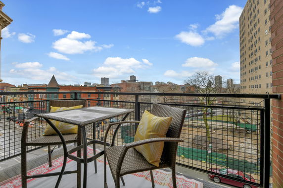 View from a balcony overlooking a cityscape with buildings and a blue sky.
