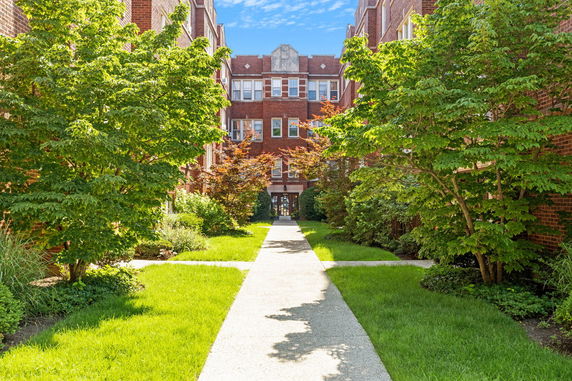 Front view of a brick apartment building with trees and walkway