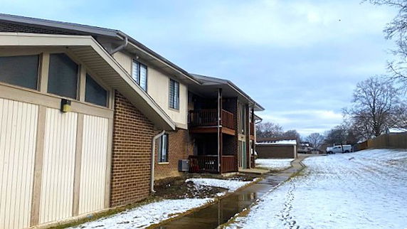 Side view of a two-story house with brick and wood paneling and an overhanging roof.