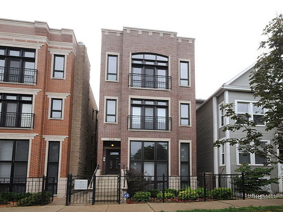 Front view of a three-story brick residential building with balconies.
