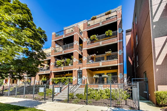 Front view of a multi-story brick apartment building with balconies and plants.